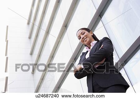 Stock Image - Businesswoman standing outdoors by building smiling (high key/selective focus). Fotosearch