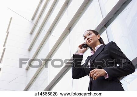 Stock Photo - Businesswoman standing outdoors by building on cellular phone (high key/selective focus). Fotosearch