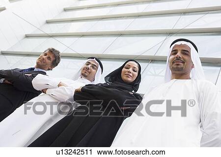 Stock Image - Four businesspeople standing outdoors by building smiling (selective focus). Fotosearch