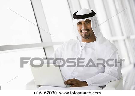 Stock Image - Man indoors with laptop smiling (high key/selective focus). Fotosearch