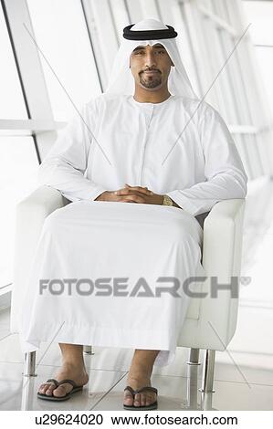 Stock Image - Man sitting indoors smiling (high key/selective focus). Fotosearch