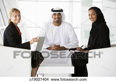 Three businesspeople indoors with a laptop smiling (high key/selective focus) View Large Photo Image Picture - Three businesspeople indoors with a laptop smiling (high key/selective focus). Fotosearch