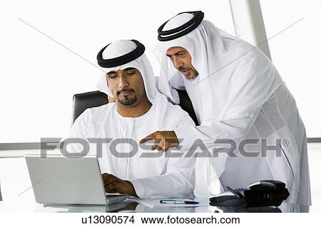 Picture - Two businessmen in office pointing at laptop (high key/selective focus). Fotosearch