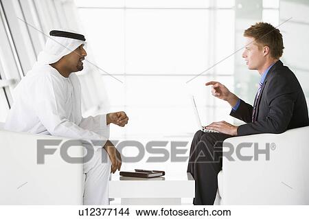 Two businessmen indoors with a laptop talking and smiling (high key/selective focus) View Large Photo Image Picture - Two businessmen indoors with a laptop talking and smiling (high key/selective focus). Fotosearch