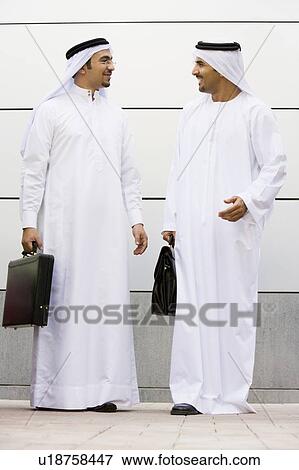 Stock Photo - Two businessmen standing outdoors with briefcases talking and smiling. Fotosearch