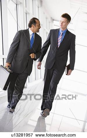 Stock Photo - Two businessmen walking in a corridor talking (high key/selective focus). Fotosearch