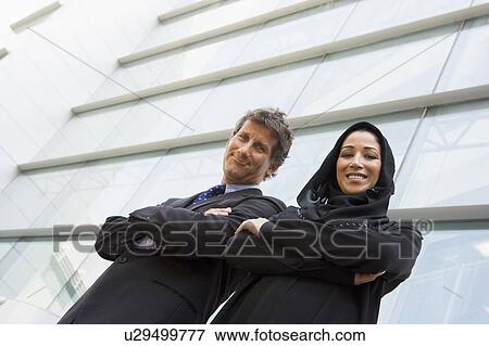 Stock Photo - Two businesspeople standing outdoors by building smiling (selective focus). Fotosearch