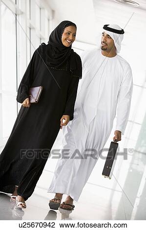 Stock Image - Two businesspeople walking in a corridor and smiling (high key/selective focus). Fotosearch