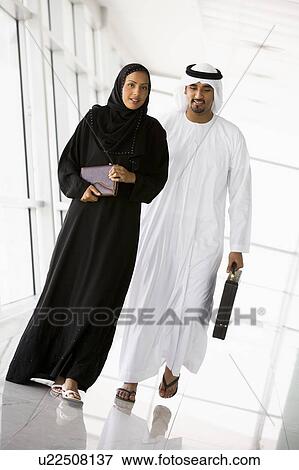 Stock Photo - Two businesspeople walking in a corridor and smiling (high key/selective focus). Fotosearch