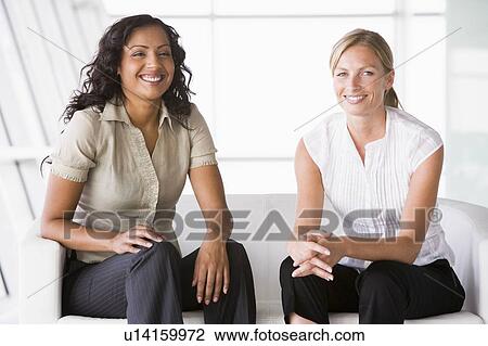 Two businesswomen sitting indoors smiling (high key/selective focus) View Large Photo Image Stock Image - Two businesswomen sitting indoors smiling (high key/selective focus). Fotosearch