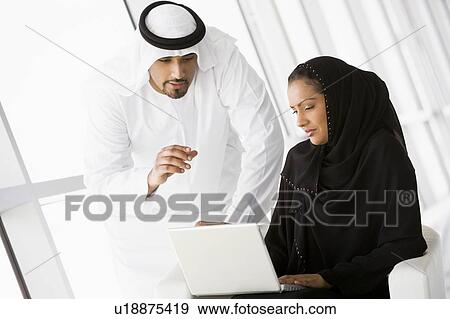 Stock Photo - Two people indoors with laptop smiling (high key/selective focus). Fotosearch