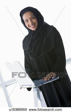Woman indoors standing with laptop and smiling (high key/selective focus) View Large Photo Image Stock Photo - Woman indoors standing with laptop and smiling (high key/selective focus). Fotosearch