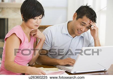 Stock Photography - Couple in dining room with laptop looking unhappy. Fotosearch