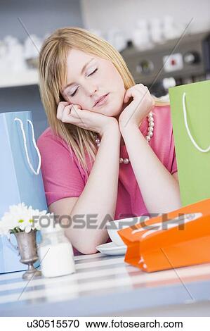 Stock Image - Exhausted young woman sitting at a table taking a break from shopping. Fotosearch