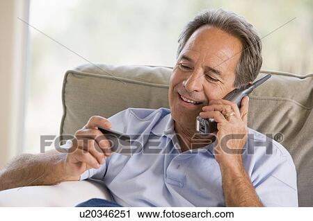 Man indoors using telephone and looking at credit card smiling View Large Photo Image Stock Image - Man indoors using telephone and looking at credit card smiling. Fotosearch