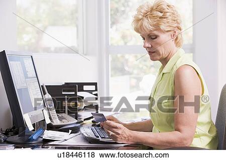 Stock Photo - Woman in home office at computer with credit card frowning. Fotosearch