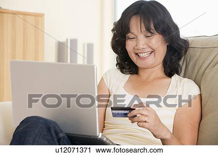 Woman in living room using laptop holding credit card and smiling View Large Photo Image Stock Image - Woman in living room using laptop holding credit card and smiling. Fotosearch