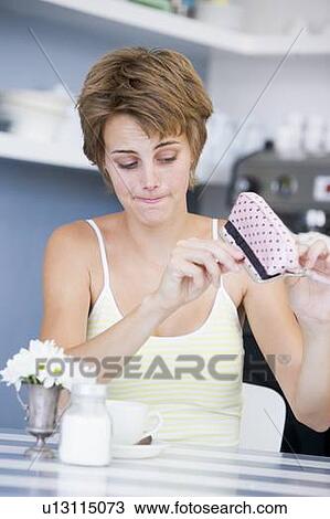Young woman sitting at a table checking change purse View Large Photo Image Stock Image - Young woman sitting at a table checking change purse. Fotosearch