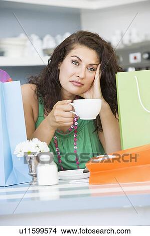 Picture - Young woman sitting at a table taking a break from shopping and drinking tea. Fotosearch