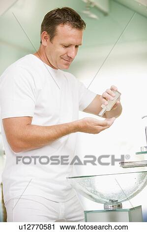 Stock Image - Man in bathroom applying aftershave and smiling. Fotosearch