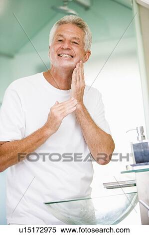 Stock Photography - Man in bathroom applying aftershave and smiling. Fotosearch