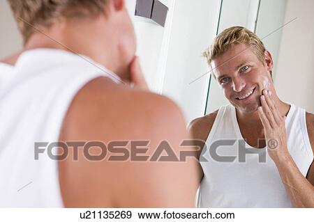 Stock Photo - Man in bathroom applying face cream smiling. Fotosearch
