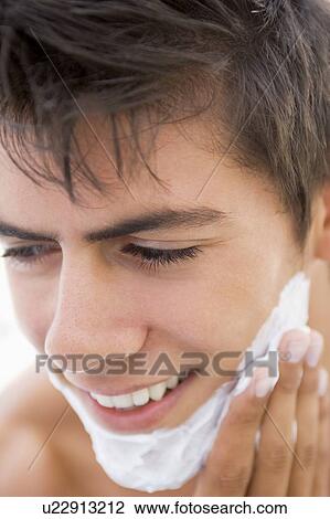 Stock Image - Man putting on shaving cream smiling. Fotosearch
