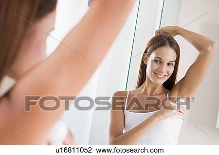 Stock Image - Woman in bathroom applying deodorant and smiling. Fotosearch