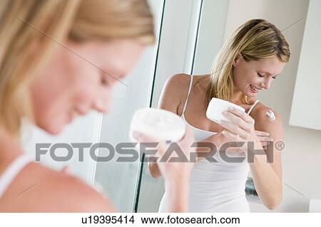 Picture - Woman in bathroom applying lotion smiling. Fotosearch