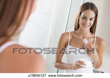 Stock Photo - Woman in bathroom applying lotion smiling. Fotosearch