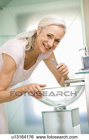 Woman in bathroom brushing teeth smiling View Large Photo Image Stock Photograph - Woman in bathroom brushing teeth smiling. Fotosearch