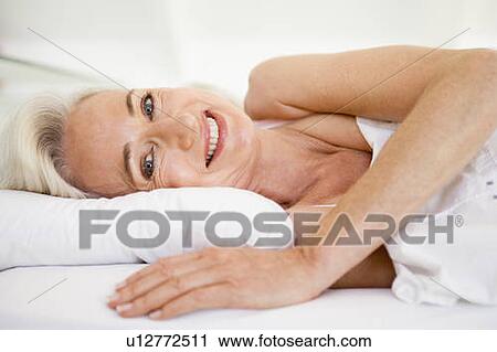 Stock Image - Woman lying in bed smiling. Fotosearch