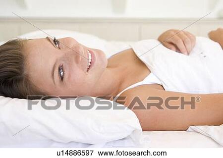 Stock Photo - Woman lying in bed smiling. Fotosearch