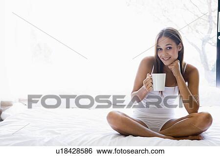 Woman sitting on bed drinking coffee smiling View Large Photo Image Stock Photograph - Woman sitting on bed drinking coffee smiling. Fotosearch