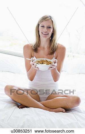 Woman sitting on bed eating cereal smiling View Large Photo Image Stock Image - Woman sitting on bed eating cereal smiling. Fotosearch