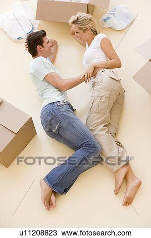 Stock Image - Couple lying on floor by open boxes in new home smiling. Fotosearch