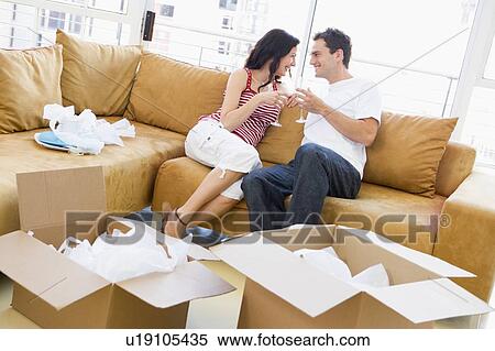 Couple relaxing with champagne by boxes in new home smiling View Large Photo Image Stock Photography - Couple relaxing with champagne by boxes in new home smiling. Fotosearch
