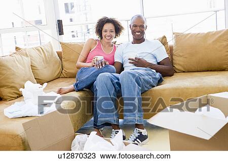 Stock Image - Couple relaxing with coffee by boxes in new home smiling. Fotosearch
