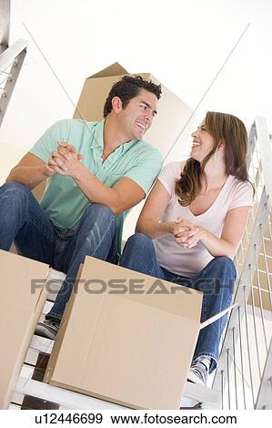 Stock Photo - Couple sitting on staircase with boxes in new home smiling. Fotosearch
