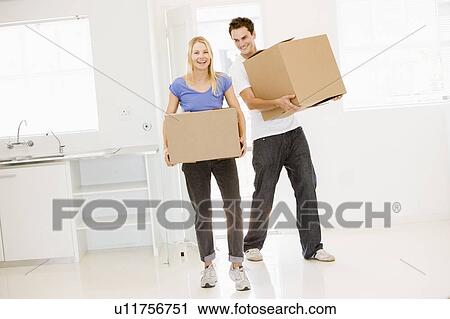 Stock Image - Couple with boxes moving into new home smiling. Fotosearch