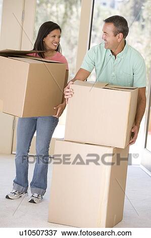 Stock Photo - Couple with boxes moving into new home smiling. Fotosearch