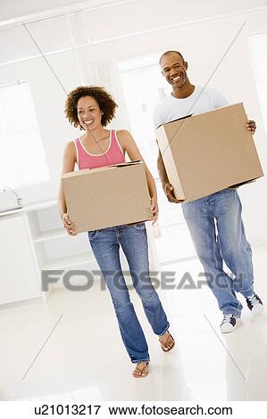 Stock Photo - Couple with boxes moving into new home smiling. Fotosearch