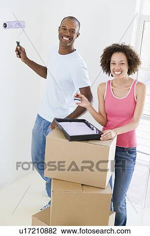 Stock Image - Couple with roller and paint in new home smiling. Fotosearch