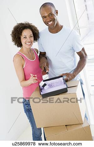 Couple with roller and paint in new home smiling View Large Photo Image Stock Photo - Couple with roller and paint in new home smiling. Fotosearch