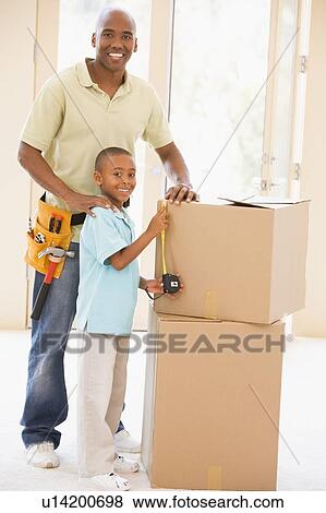 Stock Photo - Father wearing tool belt standing by son and boxes in new home smiling. Fotosearch