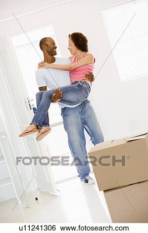 Stock Photograph - Husband holding wife in new home smiling. Fotosearch