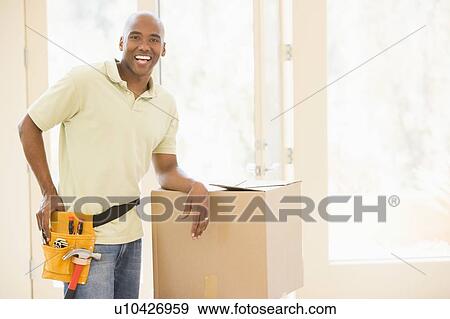 Man wearing tool belt standing by boxes in new home smiling View Large Photo Image Stock Photo - Man wearing tool belt standing by boxes in new home smiling. Fotosearch