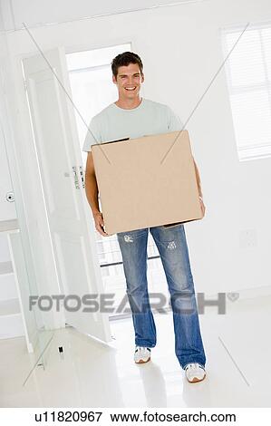 Stock Photo - Man with box moving into new home smiling. Fotosearch