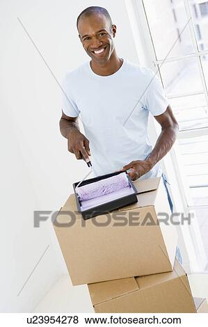 Stock Photo - Man with roller and paint in new home smiling. Fotosearch
