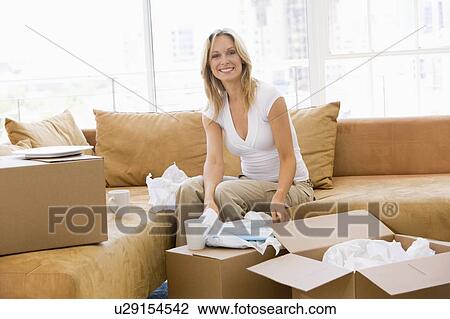 Stock Image - Woman unpacking boxes in new home smiling. Fotosearch